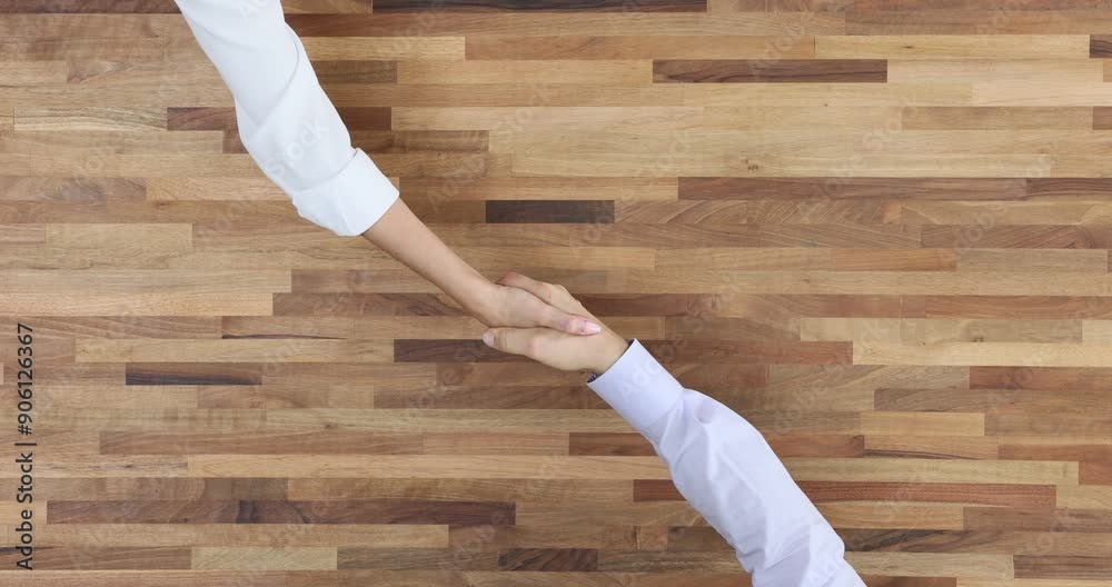 Two people shaking hands at wooden table top view