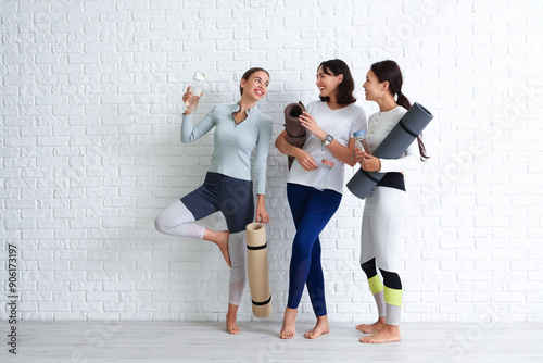 Bild auf Leinwand Sporty young women with yoga mats and water bottles near white brick wall