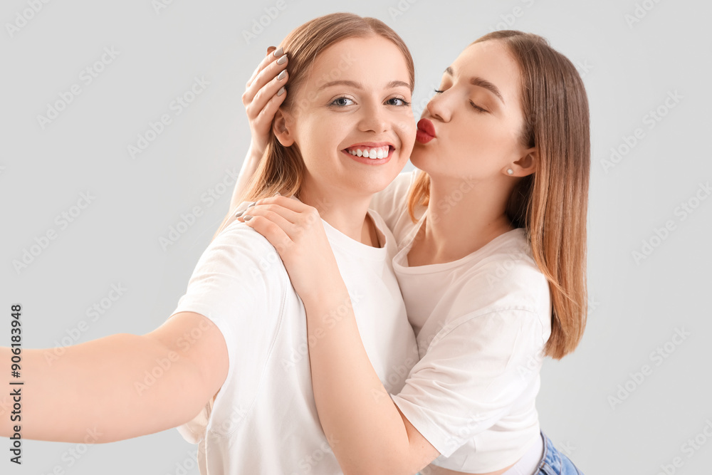 Young lesbian couple taking selfie on light background, closeup Young lesbian couple taking selfie on light background, closeup