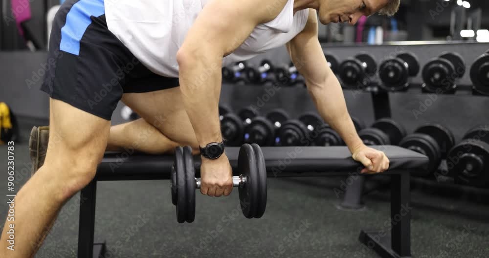 Young man performs dumbbell row exercise in modern gym slow motion. Athlete improves upper body enhancing posture during workout in club