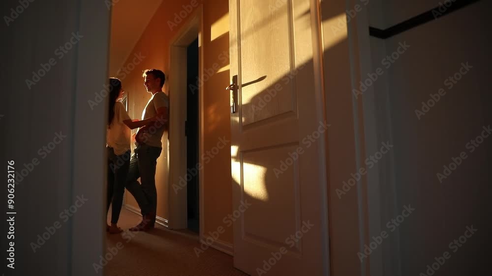 Happy young couple in love hugging, embracing, bonding each other, and kissing while standing in the corridor at their own house on the sunset background. Family and relationship