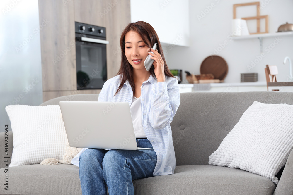 Young Asian businesswoman with laptop talking by mobile phone on sofa at home Young Asian businesswoman with laptop talking by mobile phone on sofa at home