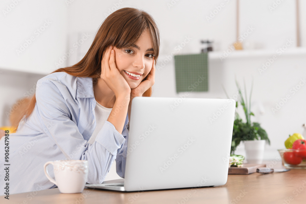 Young woman with laptop on table in kitchen