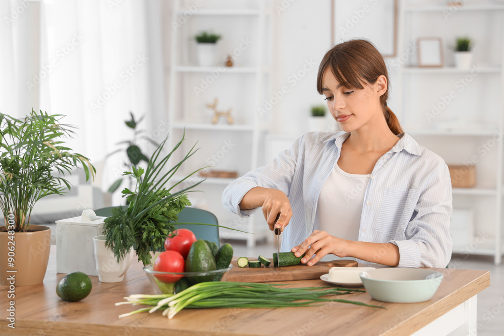 Young woman cutting cucumber at table in dining room Young woman cutting cucumber at table in dining room