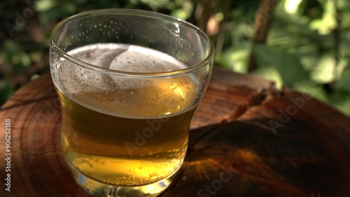 A big beer glass on a wooden table. A cold glass of beer under random sunbeams. A fresh beverage outdoors. A close-up of a beer jar.