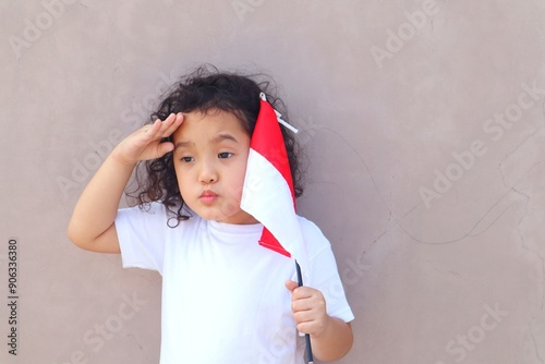 Portrait of a girl holding a red and white Indonesian flag with an adorable expression while saluting to celebrate Indonesia's independence. photo