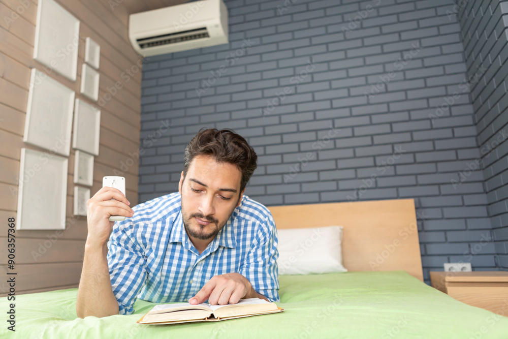 A man turns on the air conditioner on a hot summer day while reading a book, preparing for the new school year at university A man turns on the air conditioner on a hot summer day while reading a book, preparing for the new school year at university