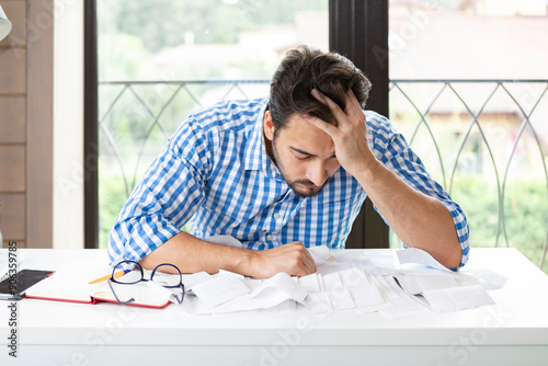 Close up of unhappy man sitting at the table, stressed and confused by calculate expense from invoice or bills, have no money to pay mortgage or loan. High prices and spending money concept photo