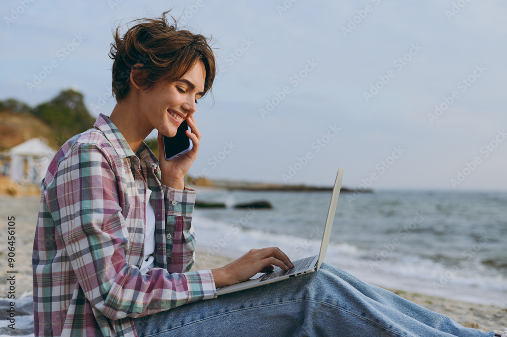 © ViDi Studio - Young IT woman wear shirt casual clothes work hold use laptop pc computer speak on mobile cell phone sits rest on sea ocean sand shore beach outdoor seaside in summer day free time. Lifestyle concept. © ViDi Studio - Young IT woman wear shirt casual clothes work hold use laptop pc computer speak on mobile cell phone sits rest on sea ocean sand shore beach outdoor seaside in summer day free time. Lifestyle concept.