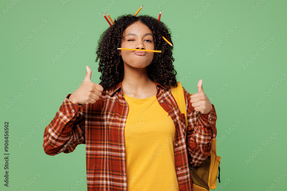Young teen girl student wear brown yellow casual clothes backpack bag with pencil in hair hold pen pov mustache sho thumb up like isolated on plain green color background. High school college concept. Young teen girl student wear brown yellow casual clothes backpack bag with pencil in hair hold pen pov mustache sho thumb up like isolated on plain green color background. High school college concept.