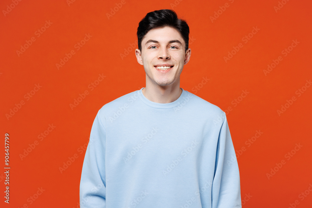 Young smiling cheerful fun satisfied cool happy Caucasian man he wears blue sweatshirt casual clothes looking camera isolated on plain red orange color background studio portrait. Lifestyle concept. Young smiling cheerful fun satisfied cool happy Caucasian man he wears blue sweatshirt casual clothes looking camera isolated on plain red orange color background studio portrait. Lifestyle concept.