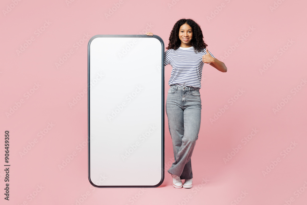 Full body little kid teen girl wears blue t-shirt casual clothes big huge blank screen mobile cell phone smartphone with area show thumb up isolated on plain pastel pink background. Childhood concept. Full body little kid teen girl wears blue t-shirt casual clothes big huge blank screen mobile cell phone smartphone with area show thumb up isolated on plain pastel pink background. Childhood concept.