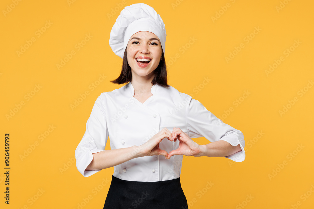 Young chef cook baker woman she wear white shirt black apron uniform toque chefs hat showing shape heart with hands heart-shape sign isolated on plain yellow background studio. Cooking food concept. Young chef cook baker woman she wear white shirt black apron uniform toque chefs hat showing shape heart with hands heart-shape sign isolated on plain yellow background studio. Cooking food concept.