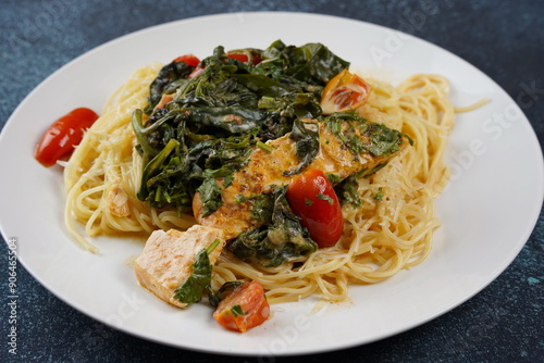 Salmon Fillet in creamy sauce with spaghetti, cream cheese and spinach and cherry tomatoes close-up on plate