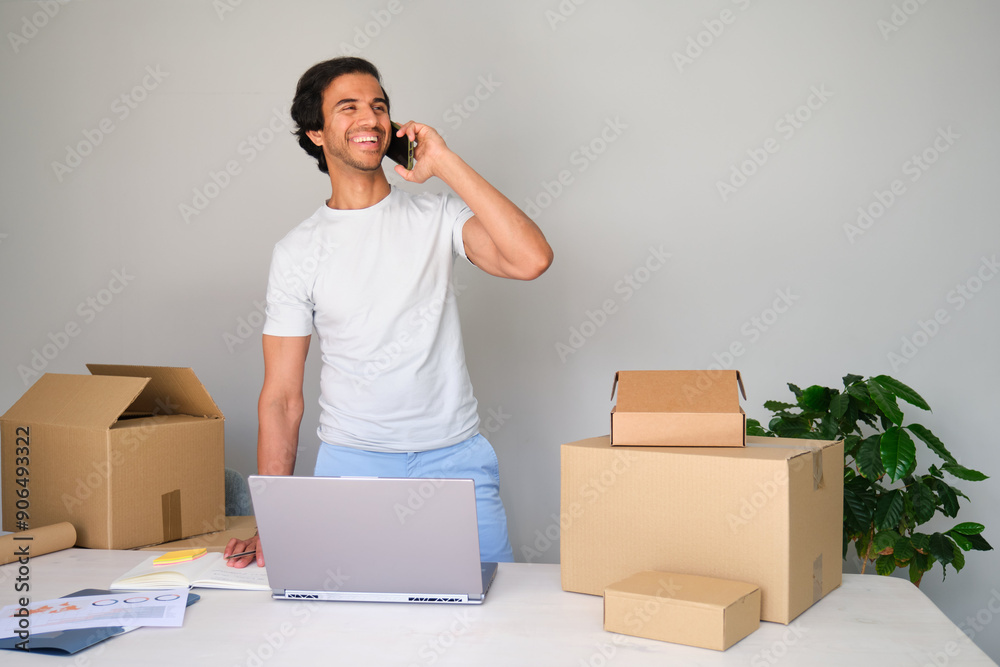 Entrepreneur is smiling while talking on the phone and managing his online business Entrepreneur is smiling while talking on the phone and managing his online business