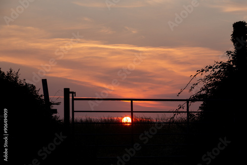 Sonnenaufgang über dem Feld hinter einem Gatter. Für den Bauer beginnt ein neuer Tag voller Arbeit.  photo