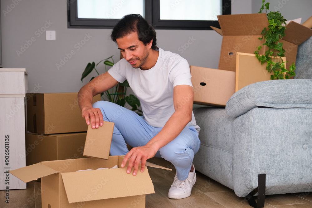 Smiling young man unpacking a cardboard box in his new apartment Smiling young man unpacking a cardboard box in his new apartment