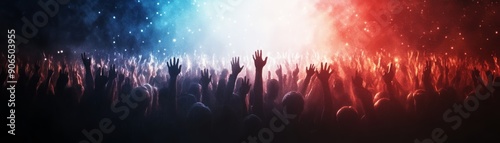 Silhouettes of a crowd of people with their arms raised, illuminated by red and blue light. © tinnakorn