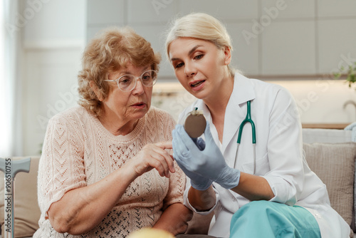 Beautiful doctor holding pacemaker explaining medical device to senior woman at home