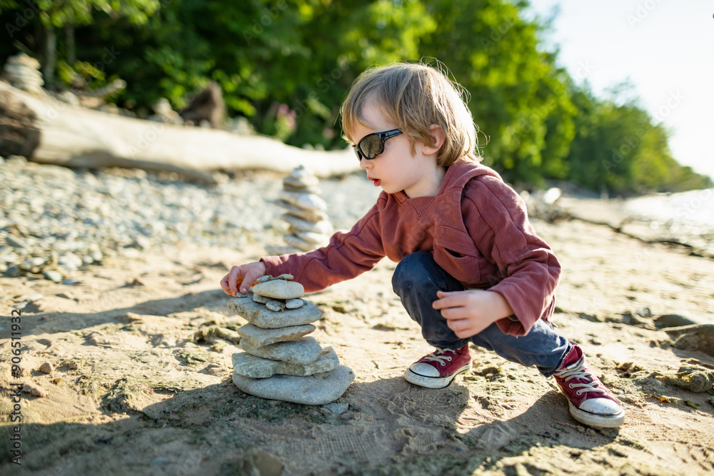 Little boy playing with balancing stones stacks on pebble beach near Valaste waterfall, reached by a wooden staircase, on the shore of Gulf of Finland, northern Estonia Little boy playing with balancing stones stacks on pebble beach near Valaste waterfall, reached by a wooden staircase, on the shore of Gulf of Finland, northern Estonia