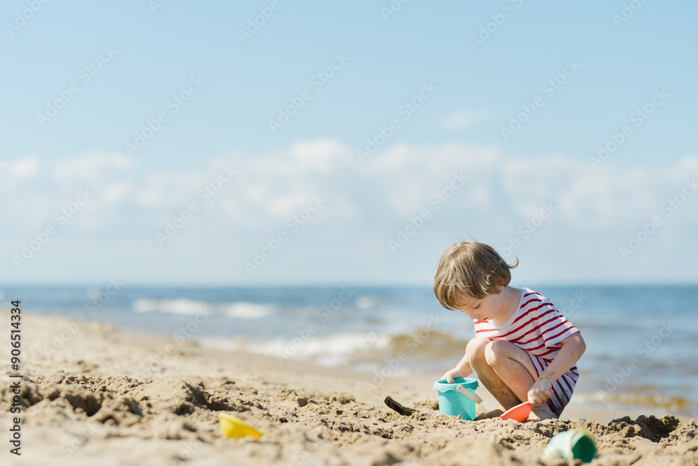 Cute little boy having fun on a sandy beach on warm and sunny summer day. Kid playing by the ocean. Summer activities for children Cute little boy having fun on a sandy beach on warm and sunny summer day. Kid playing by the ocean. Summer activities for children