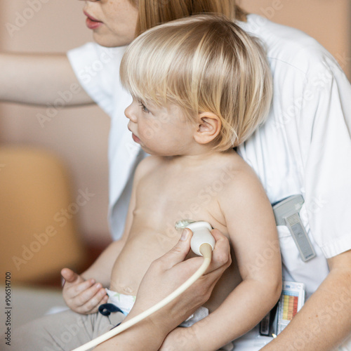 Small child being checked for heart murmur by heart ultrasound exam by cardiologist as part of regular medical checkout at pediatrician