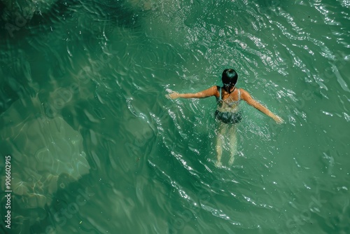 A woman is swimming in a pool of water. The water is clear and calm. The woman is wearing a black swimsuit and a black top