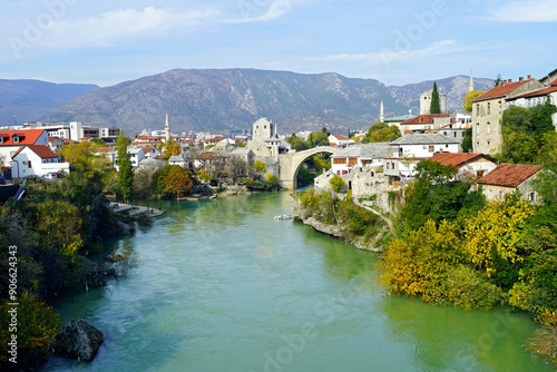 View of the center of the Bosnian Herzegovinian city of Mostar: Neretva, buildings on the banks of the river, the famous Old Bridge and mountains in the distance. Cityscape from the Lučki most bridge photo