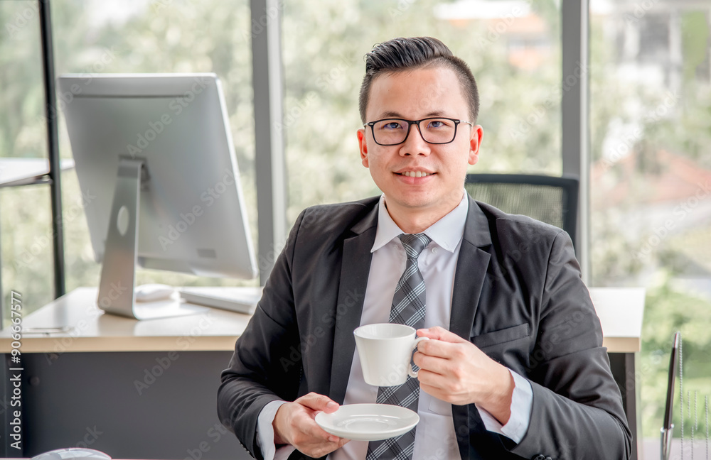 Smiling businessman in suit and glasses holding a cup in modern office, symbolizing success and relaxation in a professional environment. Smiling businessman in suit and glasses holding a cup in modern office, symbolizing success and relaxation in a professional environment.