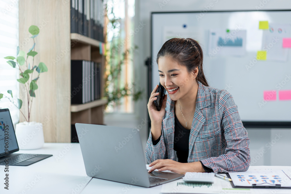 A woman is talking on her cell phone while sitting at a desk with a laptop A woman is talking on her cell phone while sitting at a desk with a laptop