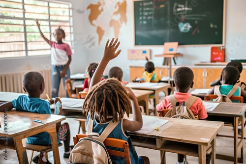 A schoolboy raises his hand up sitting at a desk in the background of a classroom with other students