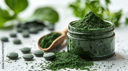 Close-up of green spirulina powder in a jar with tablets and a wooden spoon on a white surface, showcasing its natural health benefits. photo