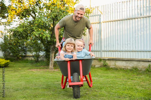 Father pushing wheelbarrow with his kid outdoors photo