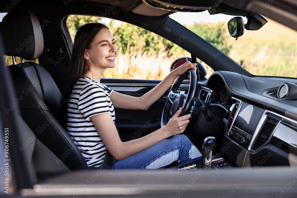 Smiling young woman holding steering wheel while driving car, view from outside Smiling young woman holding steering wheel while driving car, view from outside