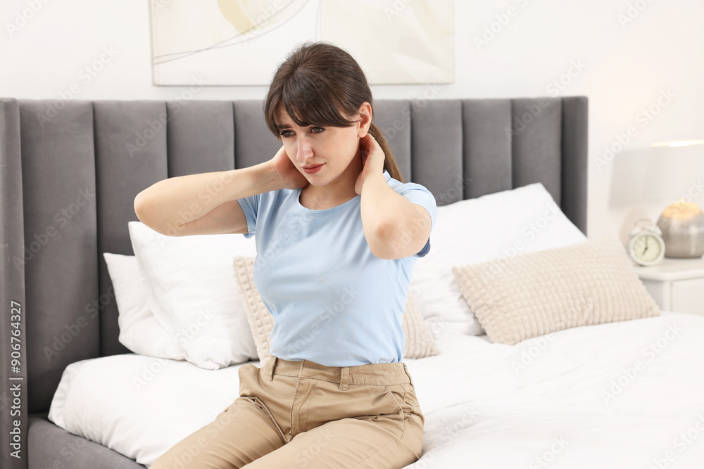 Upset woman suffering from neck pain on bed at home Upset woman suffering from neck pain on bed at home