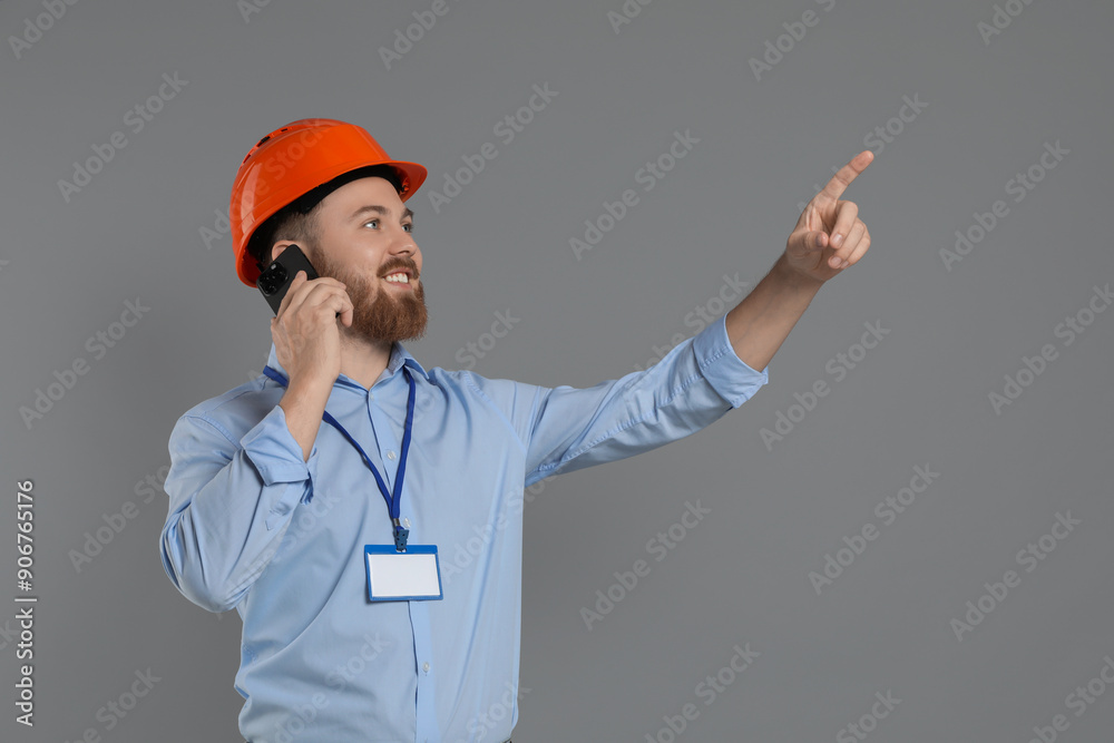 Engineer in hard hat talking on smartphone against grey background Engineer in hard hat talking on smartphone against grey background