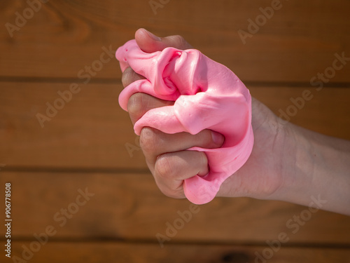 Obraz na płótnie Child hand holding and squeezing fluffy soft pink slime against brown wooden background. w salonie