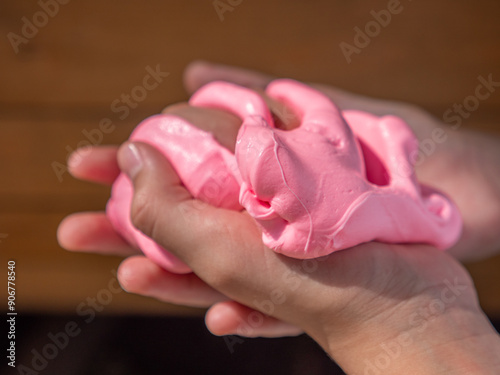 Obraz na płótnie Child hand holding and squeezing fluffy soft pink slime against brown wooden background. w salonie