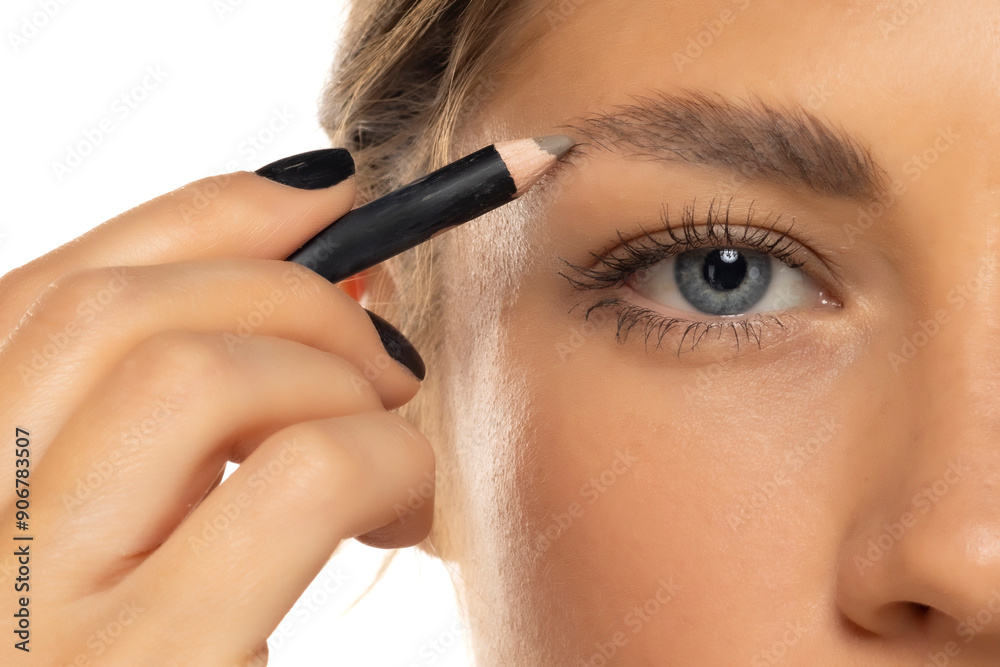 Eyebrow care up close. Cute young woman doing eyebrow styling with pencil on a white background Eyebrow care up close. Cute young woman doing eyebrow styling with pencil on a white background