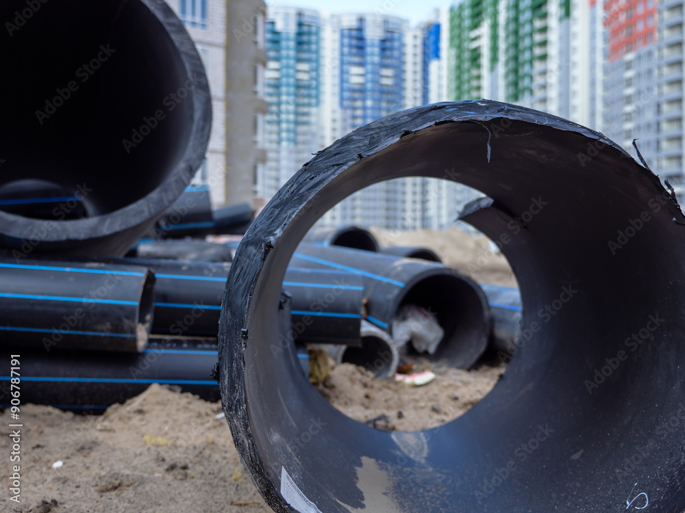 Huge black pipe in the foreground and blurry building site with new colorful high-rise buildings in the background in Kyiv, Ukraine. New district under construction concept.