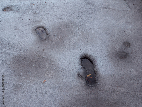 Deep footsteps embedded in wet cement and filled with water after the rain, and autumn leaf floating in it.