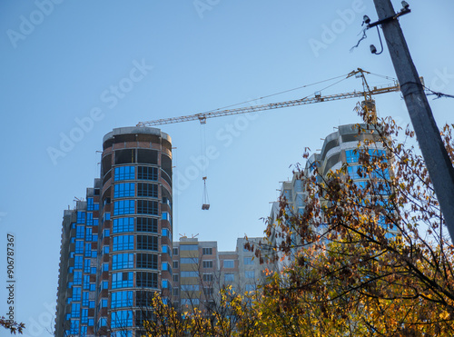 Obraz na płótnie A crane lifts a load to the new buildings at the construction site, a tree and an electric pole in the foreground. New district under construction in Kyiv, Ukraine. w salonie