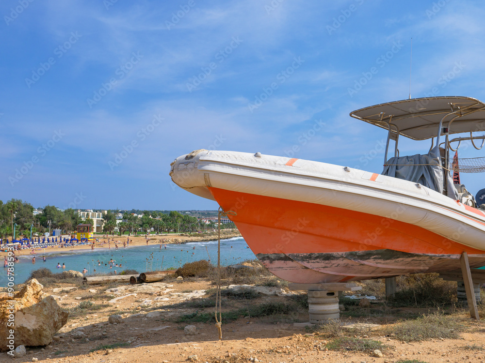Orange and white powerboat standing on tires and wooden supports at the shore in Ayia Napa. Mediterranean sea on the background.