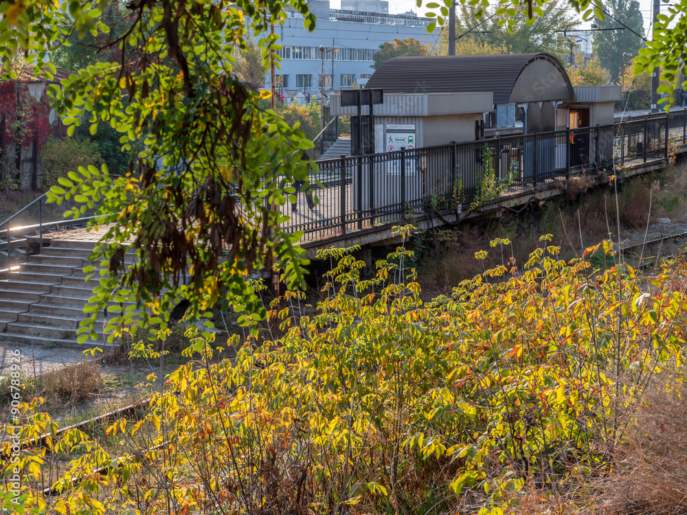 Suburban city train station with concrete platform and metal shed. Autumn colorful morning.