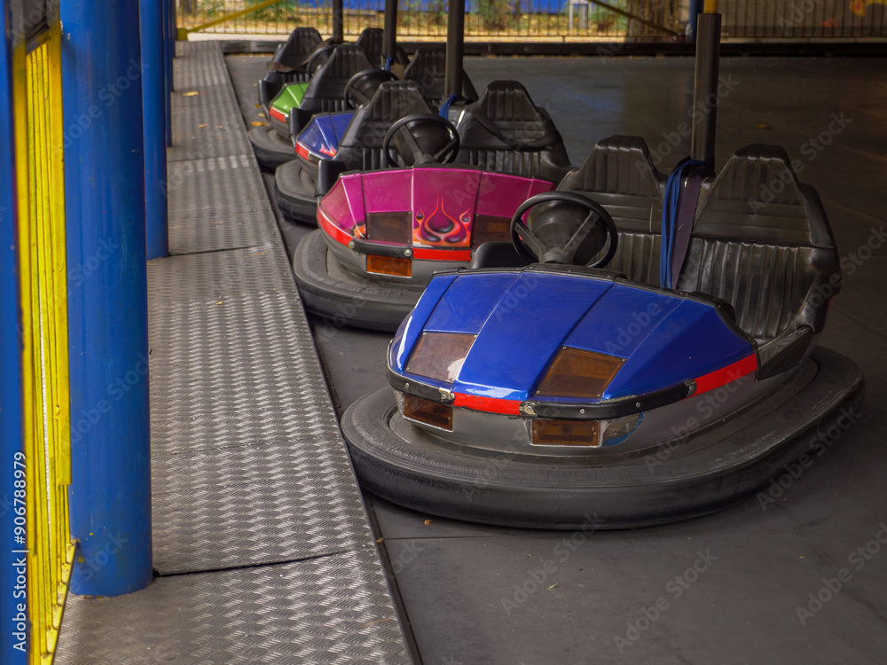 Electric colorful old-fashioned bumper cars for two standing in a row in a city amusement park. Traditional family entertainment and active leisure time outdoors.
