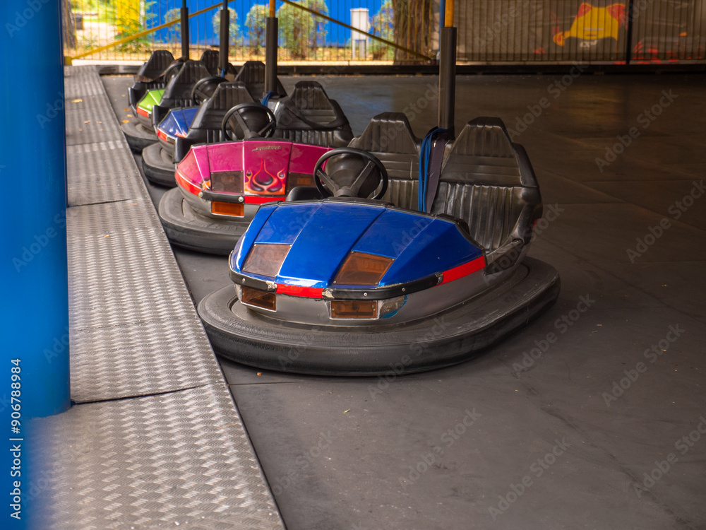 Electric colorful old-fashioned bumper cars for two standing in a row in a city amusement park. Traditional family entertainment and active leisure time outdoors.
