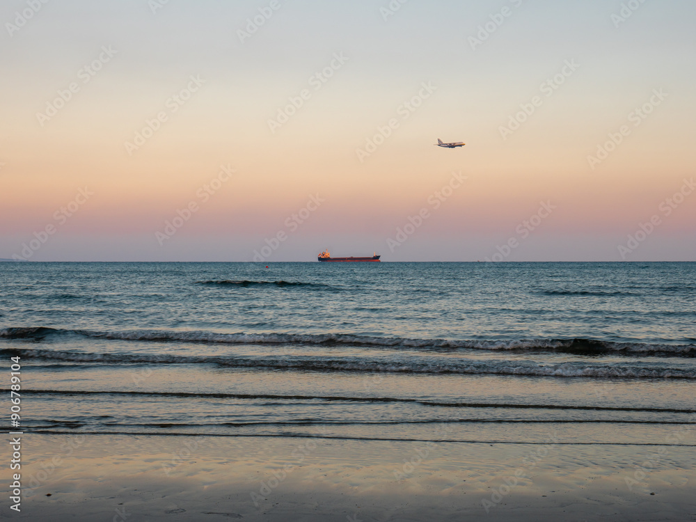 Airplane flying low above calm smooth blue Mediterranean sea with long cargo ship navigating at the horizon. Preparing to land at the airport of Larnaca, Cyprus.
