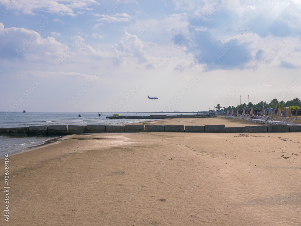 Airplane low above blue Mediterranean sea with wave breakers and sandy beach flying to Larnaca airport, Cyprus. Ships on the horizon.