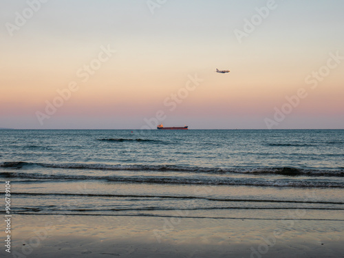Obraz na płótnie Airplane flying low above calm smooth blue Mediterranean sea with long cargo ship navigating at the horizon. Preparing to land at the airport of Larnaca, Cyprus. w salonie