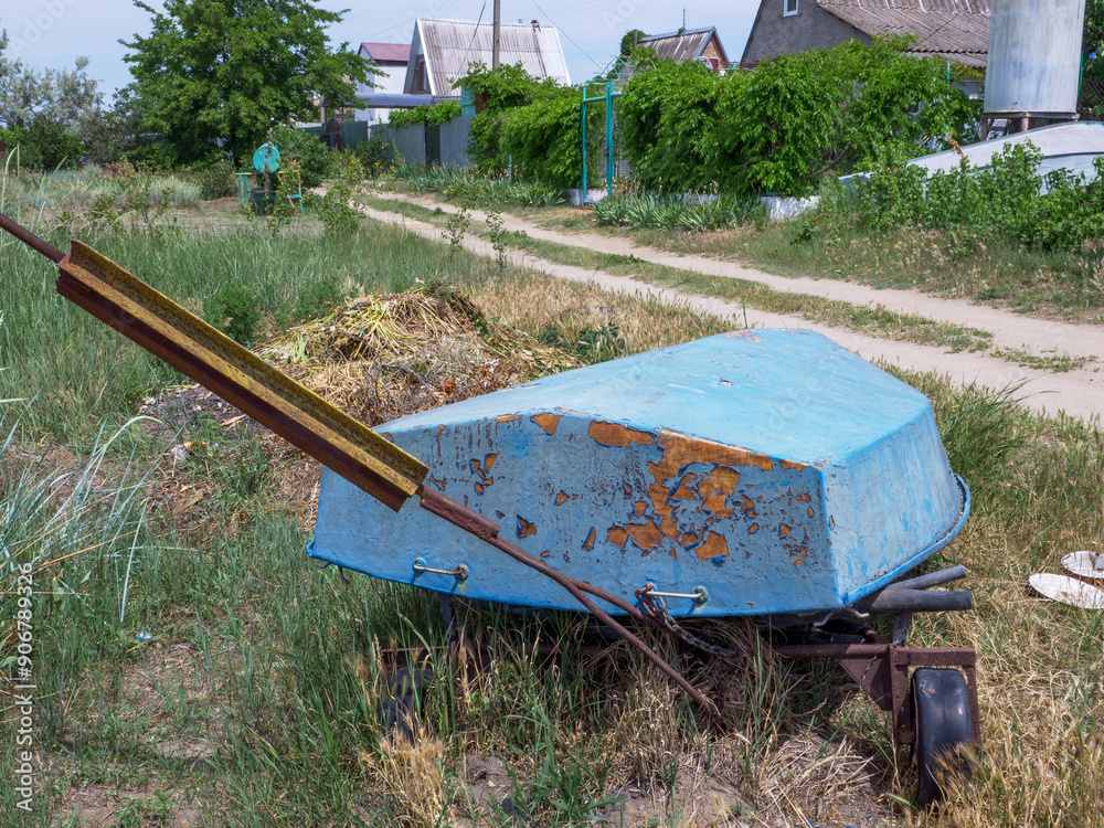 Old abandoned boat with rust and peeling off paint lays overturned upside down by the side of the country earthy road.